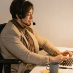 Osoba w zestawie słuchawkowym pracuje na laptopie przy biurku w świetle lampy